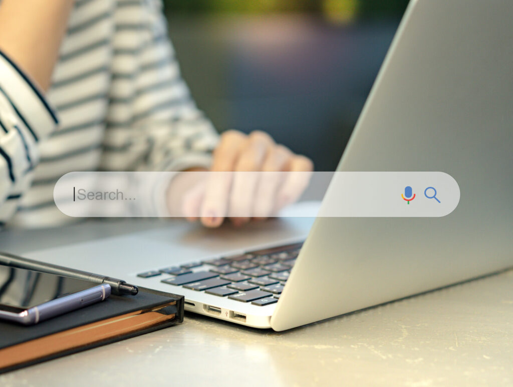 Search Engine Optimization – SEO concept Closeup of a female hands using laptop computer with a smartphone on the table Machine learning AI Artificial intelligence Smart search Keyword research
