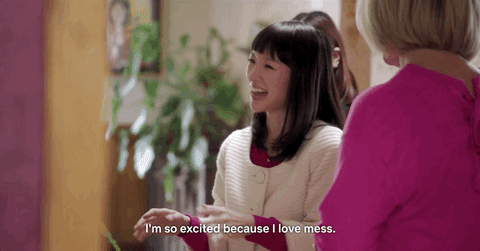 Excited Marie Kondo GIF – FSM – Digital Marketing Agency A smiling woman talks with another person in a pink sweater in a cozy room, caption reads, 'I'm so excited because I love mess.'