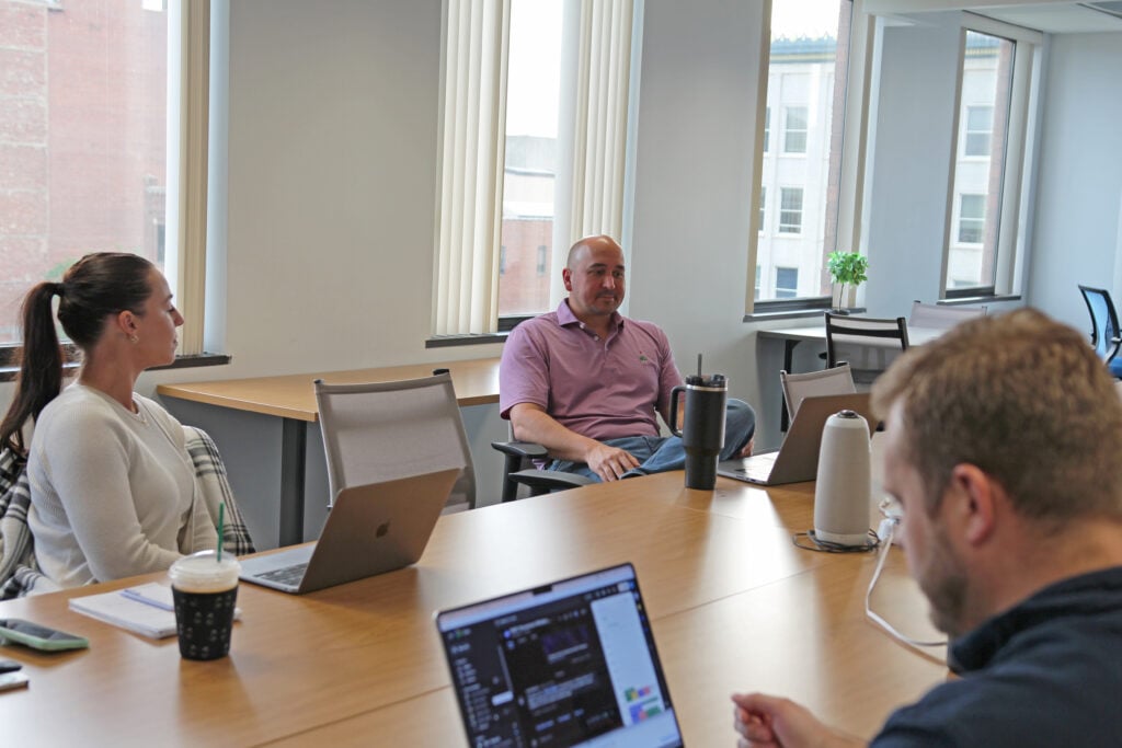 FSM_meeting_image Marketing team in a conference room reviewing campaign workflows and lead generation on laptops.