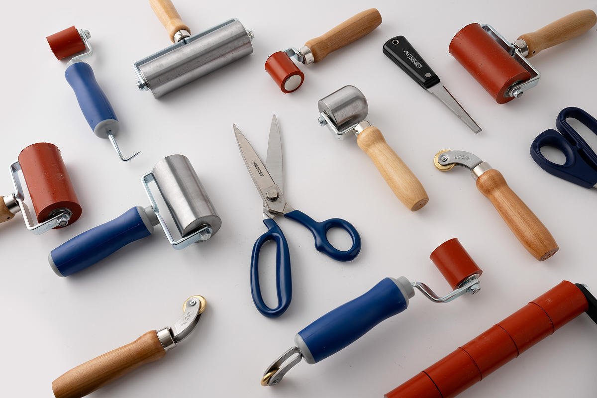 Assortment of Everhard hand tools including steel and silicone rollers, shears, and knives scattered on a white surface.
