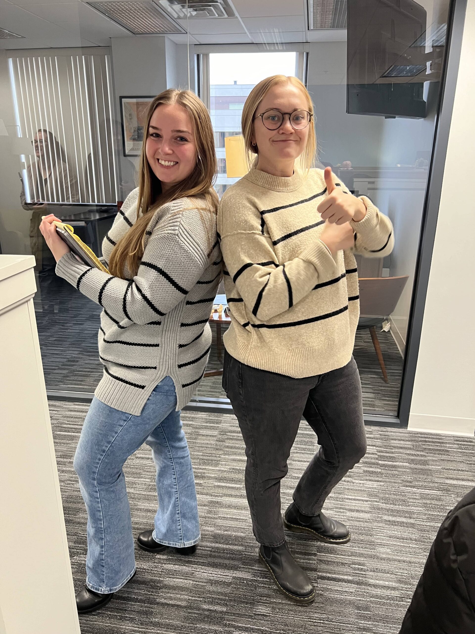 Two female colleagues pose together in an office setting.