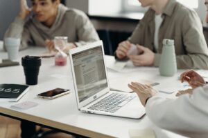 People gathered around a table in a meeting, with a laptop open and papers and drinks on the table.