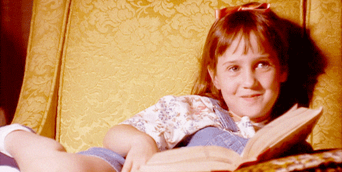 reading read GIF – FSM – Digital Marketing Agency Smiling young girl lying on a gold patterned couch, reading an open book.